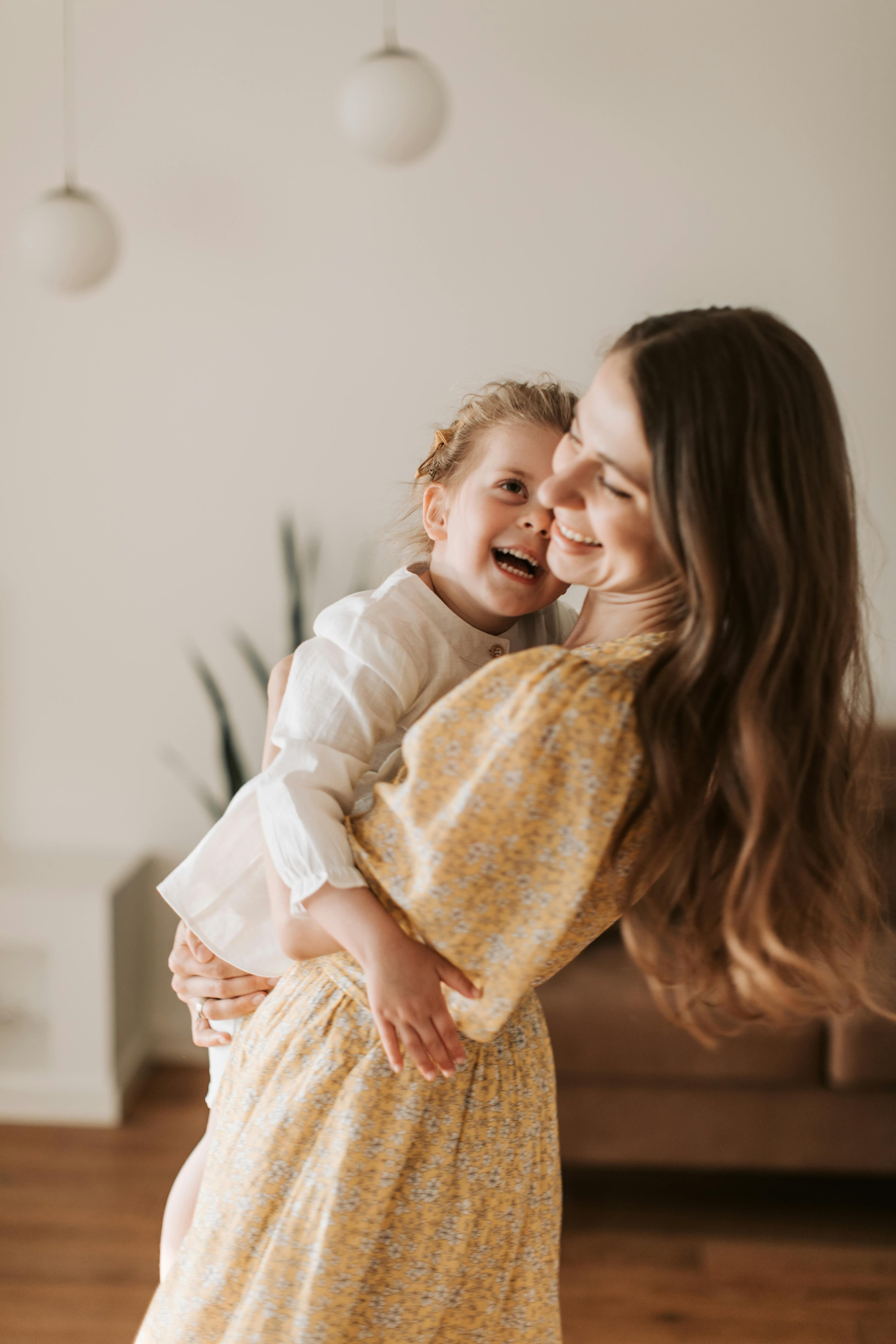A joyful mother wearing a yellow floral dress holding her laughing young daughter, capturing a moment of pure connection and happiness.